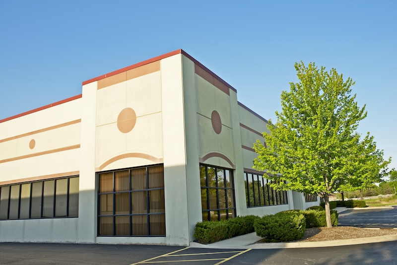 The outside of a retail building with hedges and trees around the walkways.