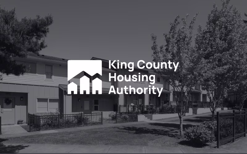 King County Housing Authority logo centered over a grayscale background of a residential housing community with trees and townhomes.