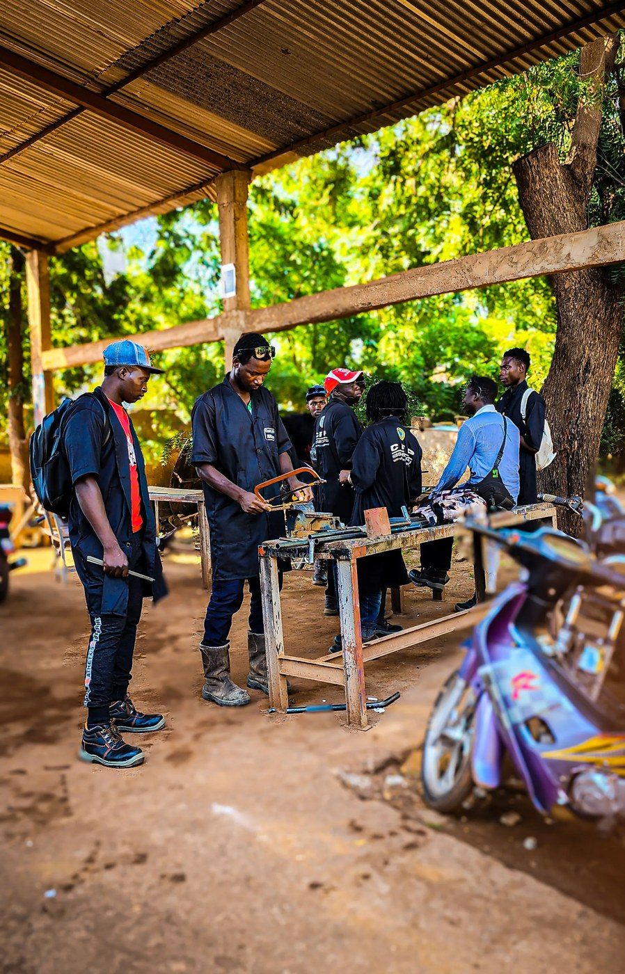 Apprenants du CFPM en séance pratique dans un atelier en plein air, autour d’un établi