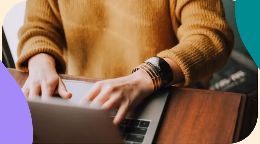 Nahaufnahme von Händen, die auf einem Laptop tippen, mit einem gemütlichen Pullover und stilvollen Armbändern.