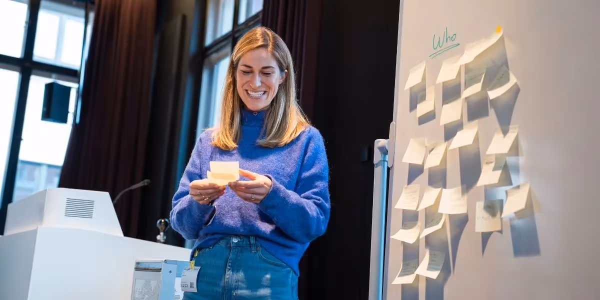 Woman smiling while reading sticky notes during an interactive workshop session.