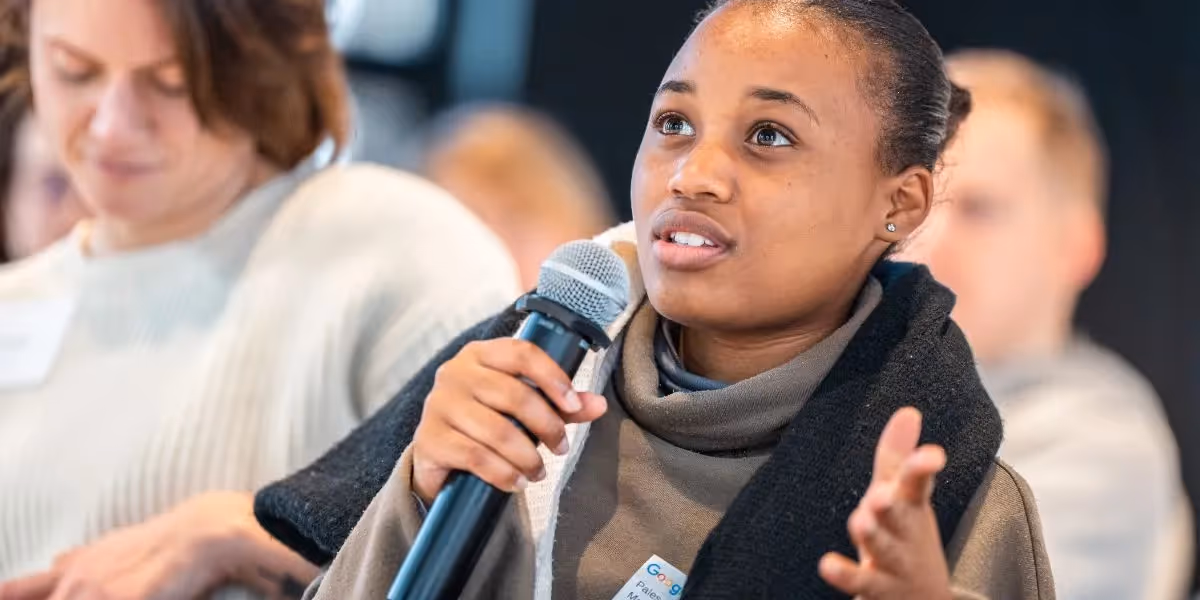 Woman holding a microphone and speaking during a classroom discussion.