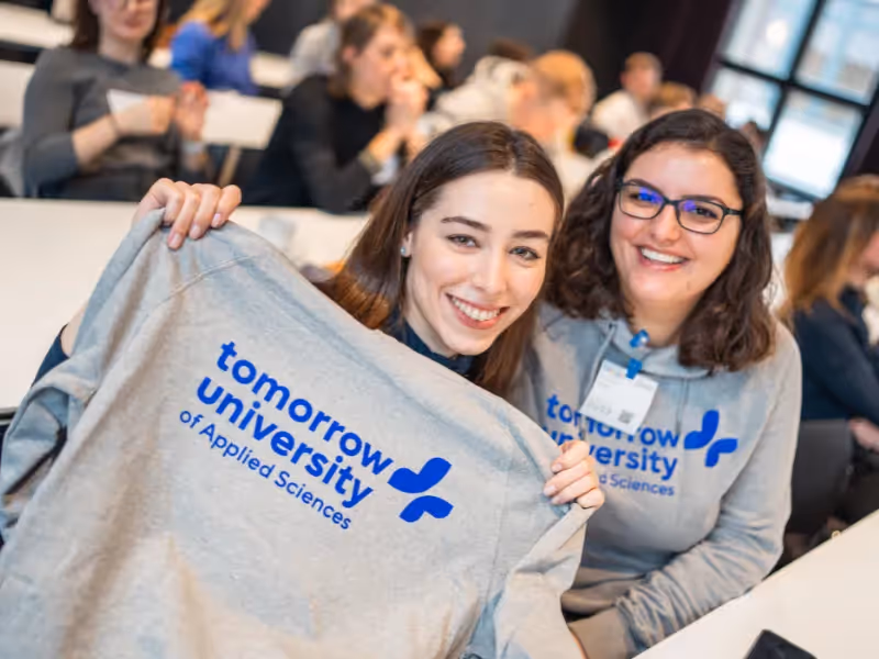 Two women smiling and holding a Tomorrow University hoodie at a classroom meetup.