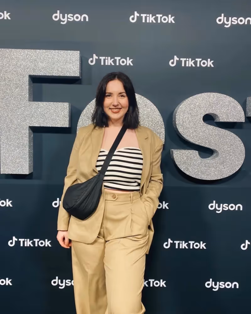 Woman in a tan suit and striped top posing in front of a TikTok and Dyson event backdrop.