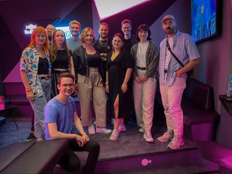 Group photo of eleven people posing in a neon-lit room with gaming screens.
