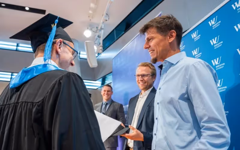 Graduate receiving diploma while shaking hands with Tomorrow University leaders
