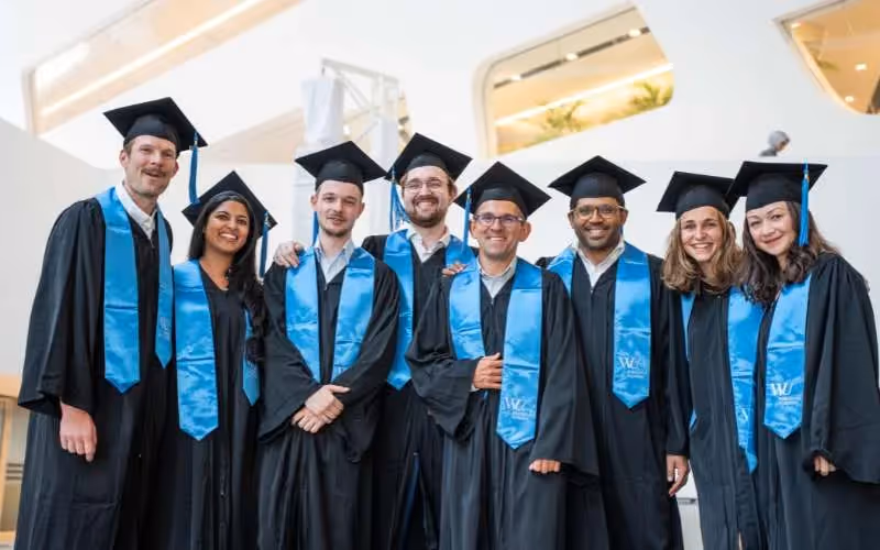 Small group of graduates smiling together in caps and gowns after the ceremony