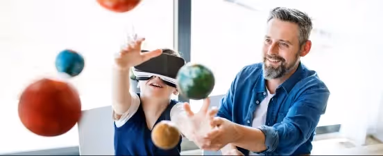 Boy with VR headset interacts with planets while smiling man guides him.