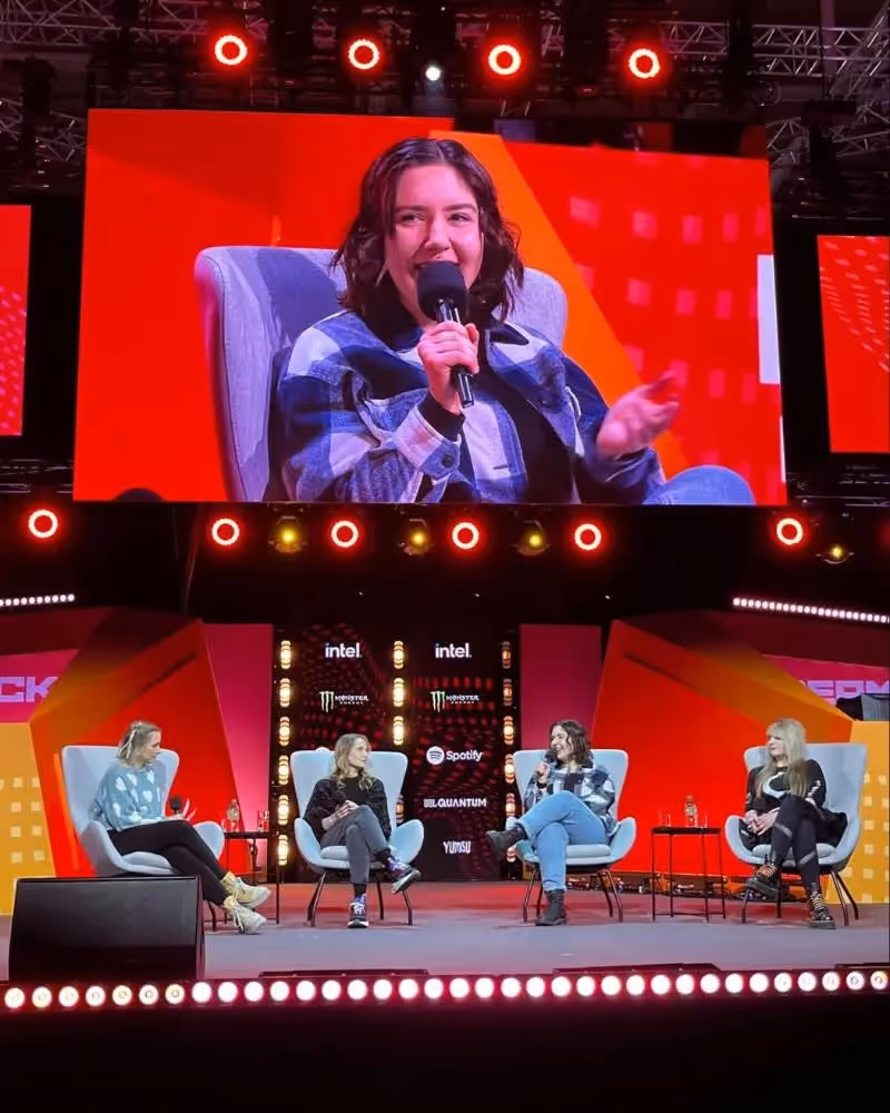 Panel discussion on a lit stage with a large screen showing a female speaker.