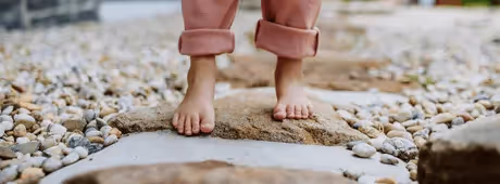 A child, only its feet are visible, walking across stones, without shoes, looking sustainable.