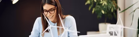 Woman smiling at desk while working near miniature wind turbines, suggesting a focus on sustainability.