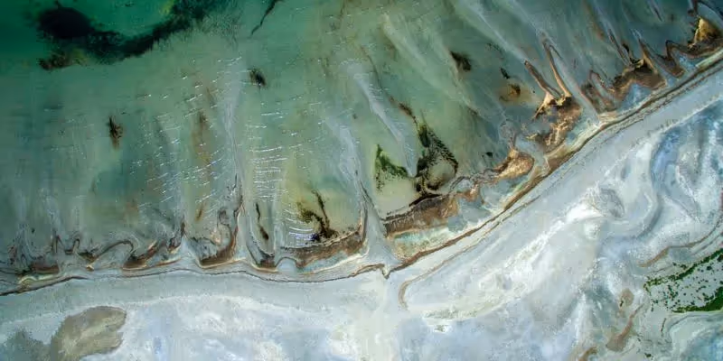 Aerial view of a coastal shoreline with green water and sand formations.
