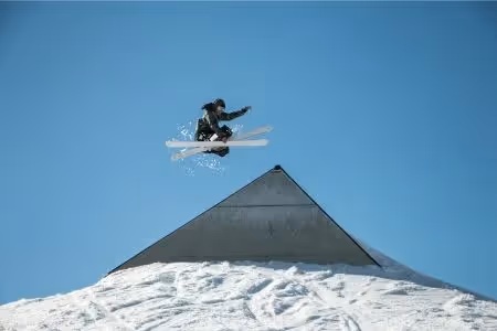 Freestyle skier mid-air above a snowy ramp with clear blue sky in the background
