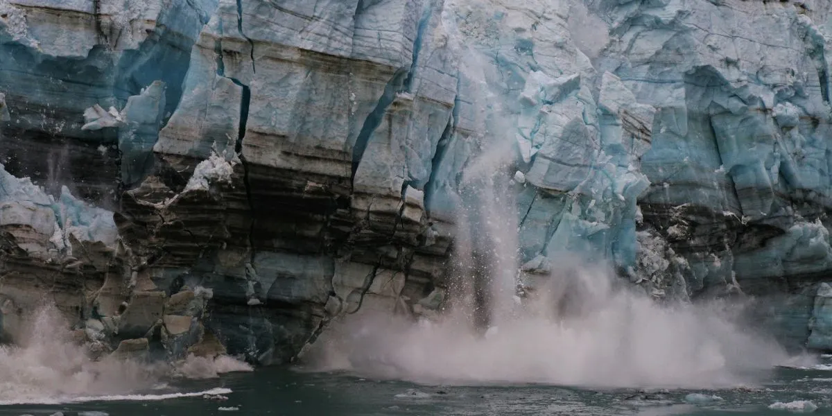 A glacier collapses into the ocean, sending ice and water splashing as it melts and breaks off near the shore.