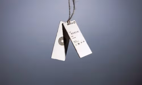 Two minimalistic white product tags hang on a string against a plain gray background, featuring simple icons and text.