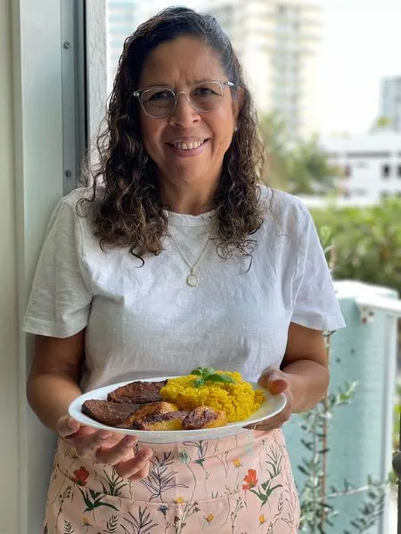 Woman smiling holding a plate of traditional food, blending tradition and innovation in Venezuelan entrepreneurship.