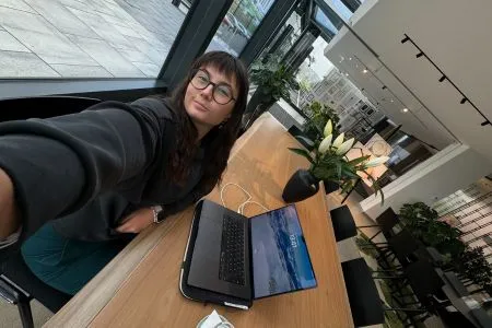 Close-up of a confident woman smiling, wearing a black turtleneck and sitting in a colorful, modern office space.
