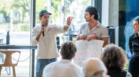Zwei Männer leiten einen Workshop, einer spricht mit Mikrofon, der andere hält ein Plakat.