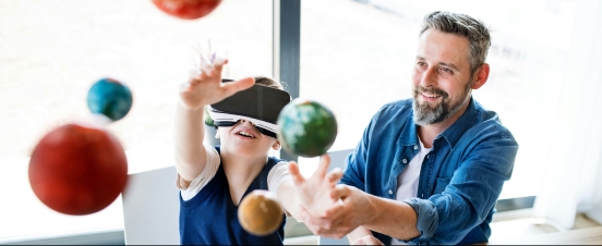 Junge mit VR-Headset interagiert mit Planeten, während ein lächelnder Mann ihn anleitet.