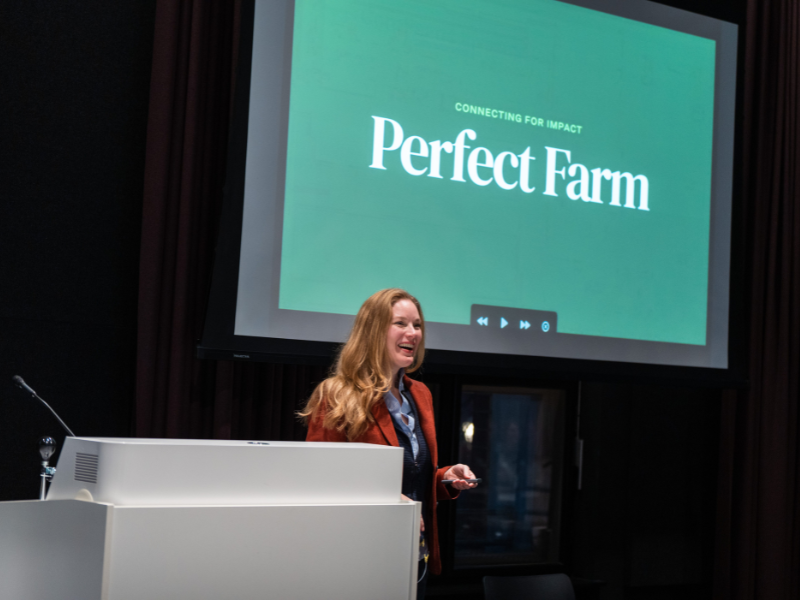 Frau präsentiert ein Projekt namens „Perfect Farm“ auf der Bühne vor einer Leinwand.