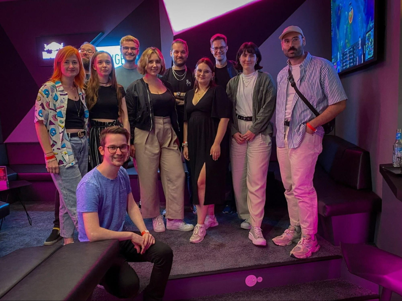 Gruppenfoto von elf Personen, die in einem neonbeleuchteten Raum mit Gaming-Bildschirmen posieren.