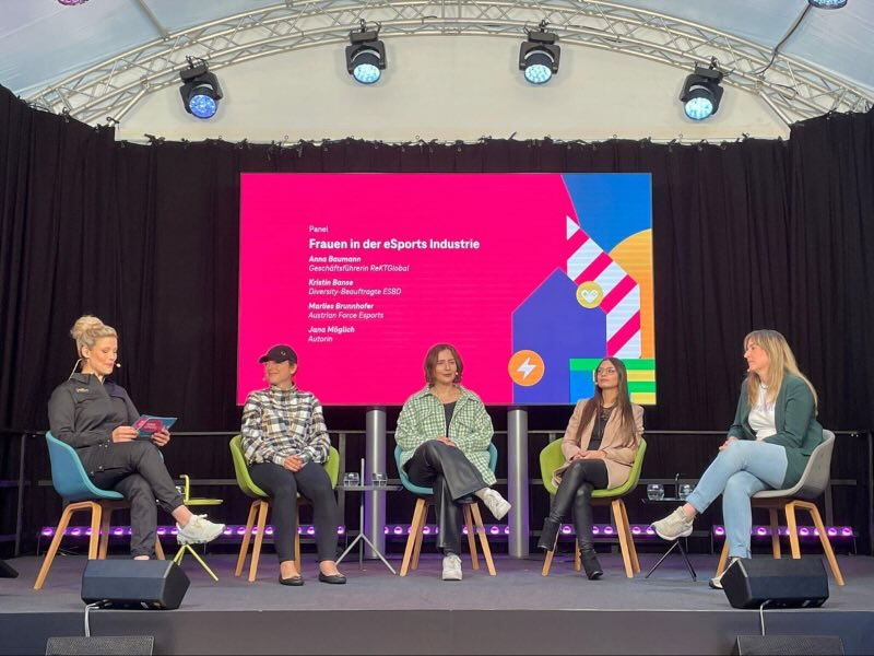 Podiumsdiskussion von fünf Frauen über die eSports-Industrie auf einer Bühne mit rotem Bildschirmhintergrund.