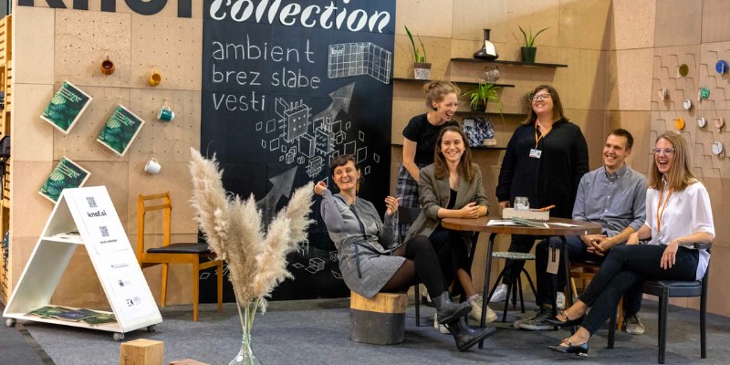 Gruppe von Menschen, die in einem Stand lächelt, während im Hintergrund der Text "knof collection" zu sehen ist.