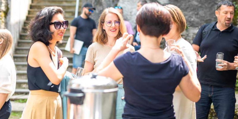 Outdoor Gruppe bei einer Unterhaltung in der Nähe von Treppen, während sie Getränke und Sonnenlicht genießen.