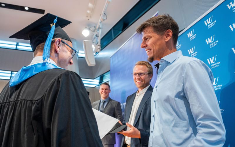 Absolvent erhält Diplom und schüttelt den Führern der Tomorrow University die Hand.