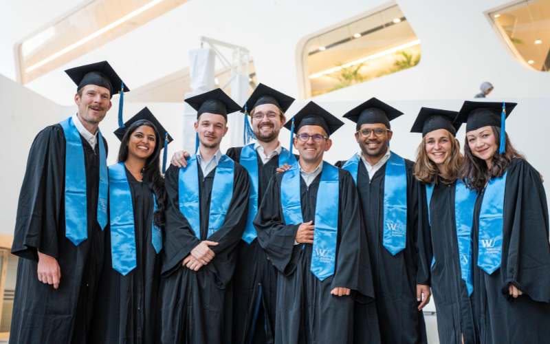 Kleine Gruppe von Absolventen lächelt nach der Zeremonie gemeinsam im Talar.