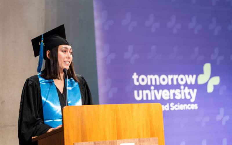 Absolvent hält Rede an einem Rednerpult mit Tomorrow University Logo im Hintergrund.