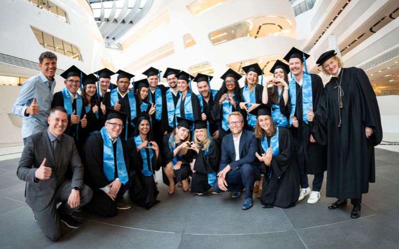 Absolventen und Dozenten feiern mit Daumen hoch und freudigen Gesten.