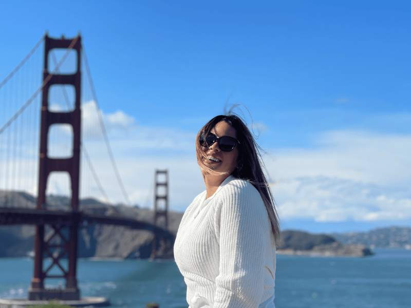 Lächelnde Frau vor der Golden Gate Bridge an einem sonnigen Tag mit klarem Himmel.