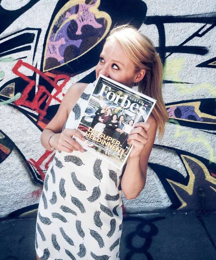 Bianca hält ein Forbes-Magazin vor einer bunten Graffitiwand.
