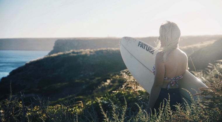 Bianca mit Surfbrett blickt auf Meeresklippen unter sanftem Morgenlicht.