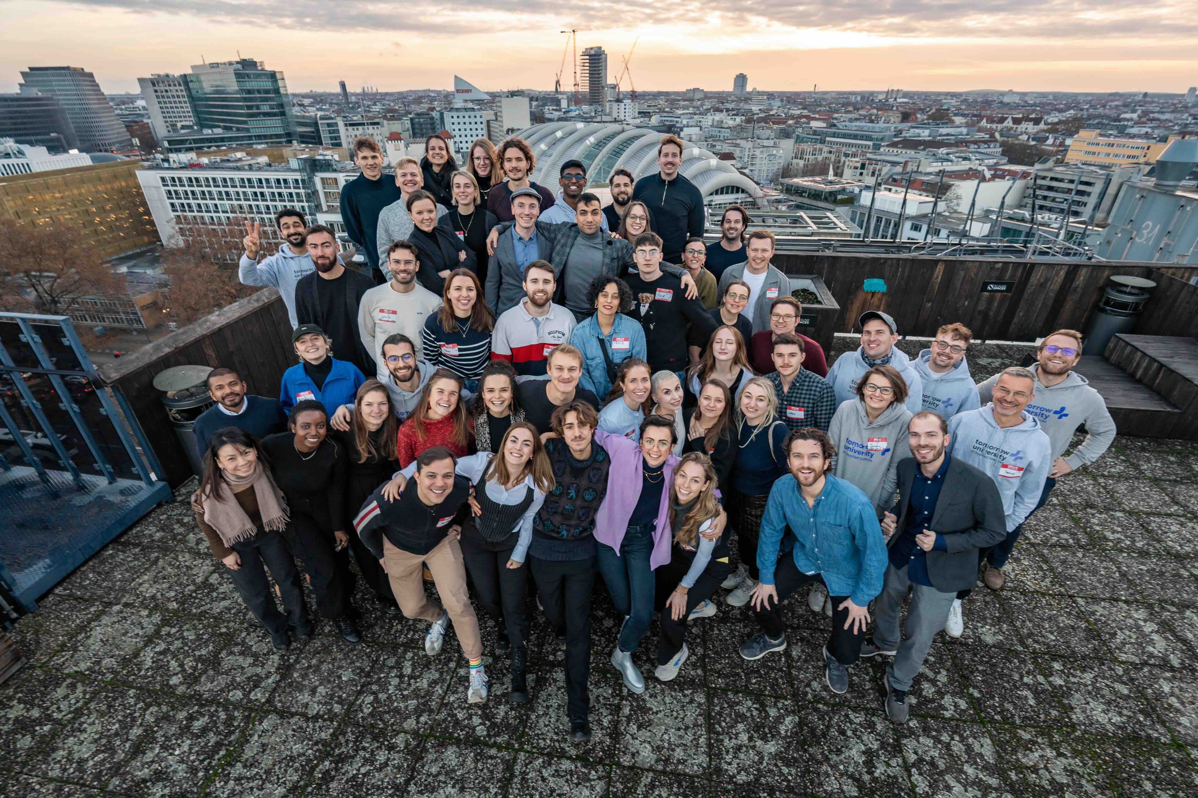 Eine große Gruppe von Lernenden der Tomorrow University posiert zusammen auf einem Dach mit Stadtlandschaft im Hintergrund
