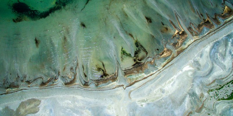 Aerial view of a coastal shoreline with green water and sand formations.