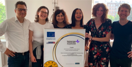 Sechs Personen lächelnd, halten ein von der EU gefördertes Projektzertifikat der Tomorrow University.