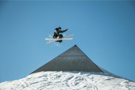 Freikünstlerin in der Luft über einer schneebedeckten Rampe mit klarem blauen Himmel im Hintergrund