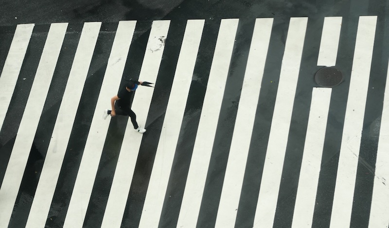 A person running across a wide striped crosswalk, seen from above on a wet street.