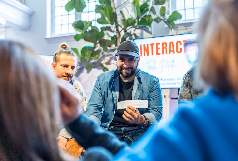 People seated in a circle during an interactive workshop, one participant holding a card while speaking to the group.