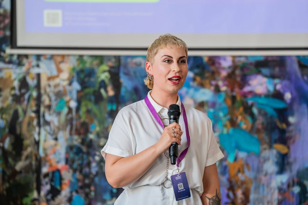 Sorana-Stefana Lehene speaks into a microphone in front of a colorful painted wall at the Berlin Immersion.