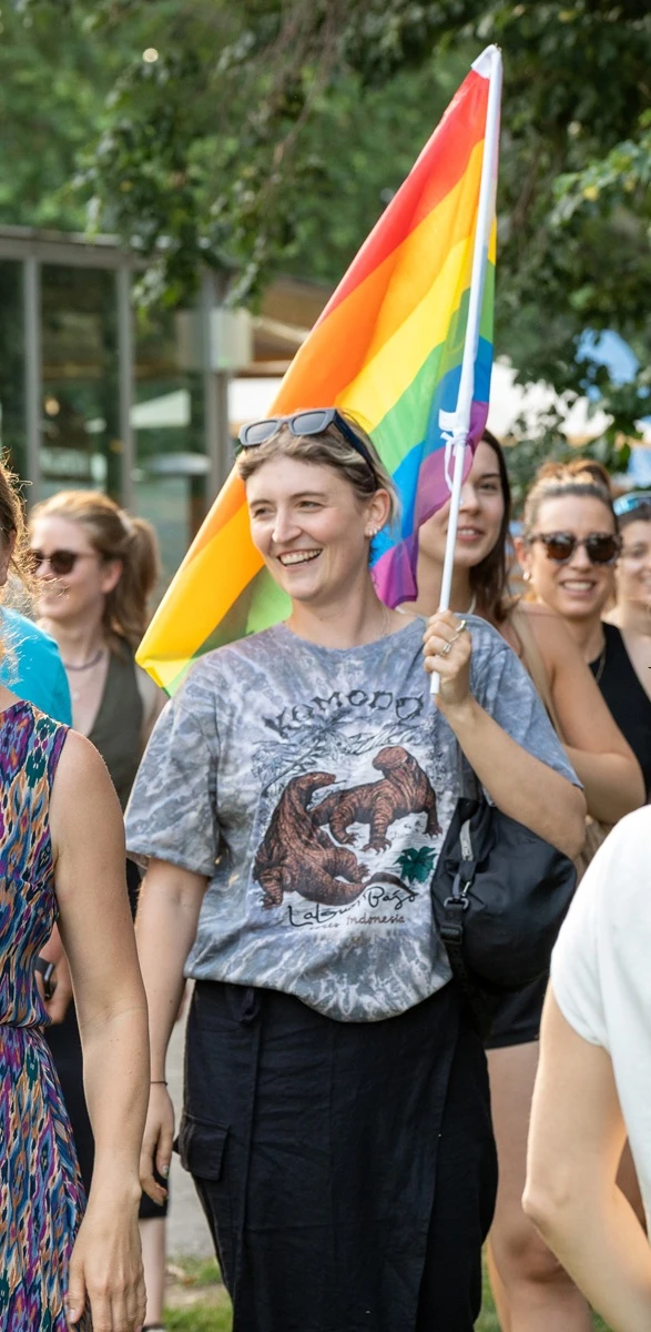 Antonia Zoe Reiter hält lachend eine Regenbogenfahne, umgeben von anderen Teilnehmenden einer Immersion in Wien.