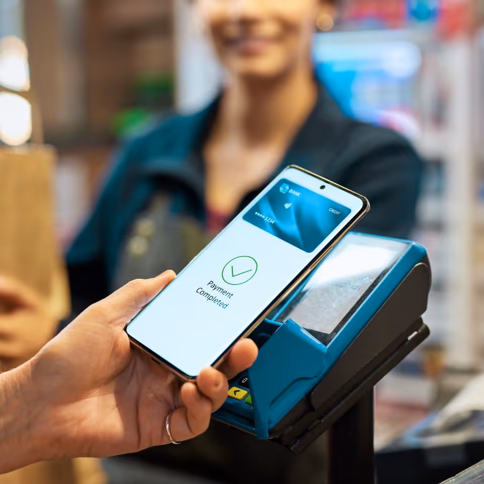 Person holding a smartphone displaying 'Payment completed' near a card payment terminal at a store.