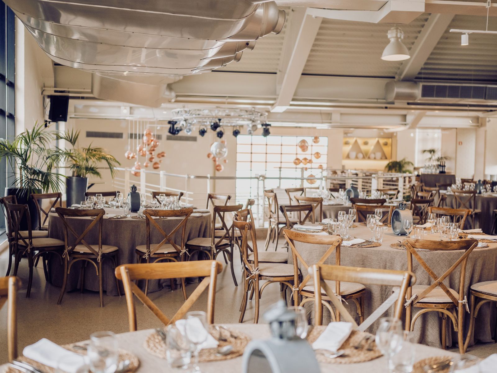 Elegant restaurant dining area with round tables set with glasses, napkins, and wooden chairs.