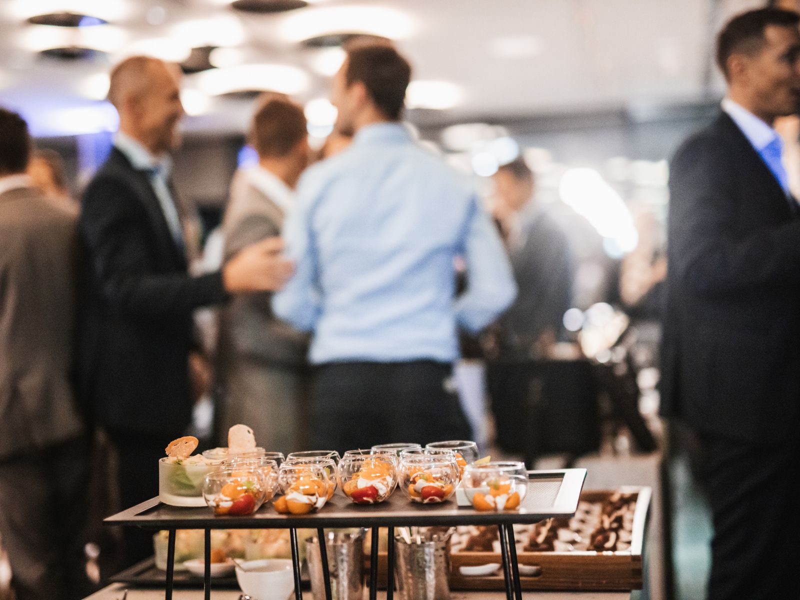 Small appetizer cups with colorful food on a tray at a social event with people mingling.