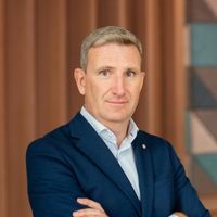 Alan Gleeson, Otonomee's CCO, in a navy blue suit with light gray hair, standing with arms crossed indoors.