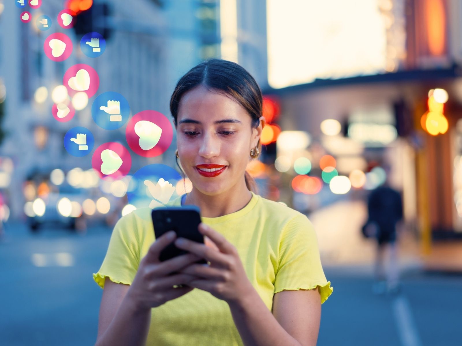 Woman in yellow shirt smiling while using smartphone with social media like and heart icons around her.
