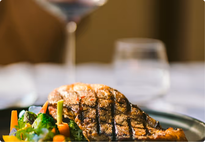 Grilled steak with mixed steamed vegetables on a dark plate.