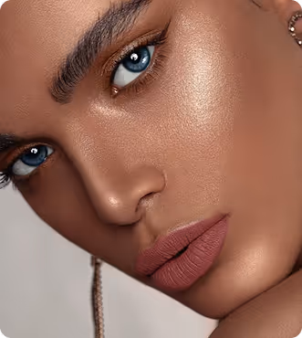 Close-up of a face with blue eyes, bold eyebrows, matte mauve lipstick, and glowing skin.